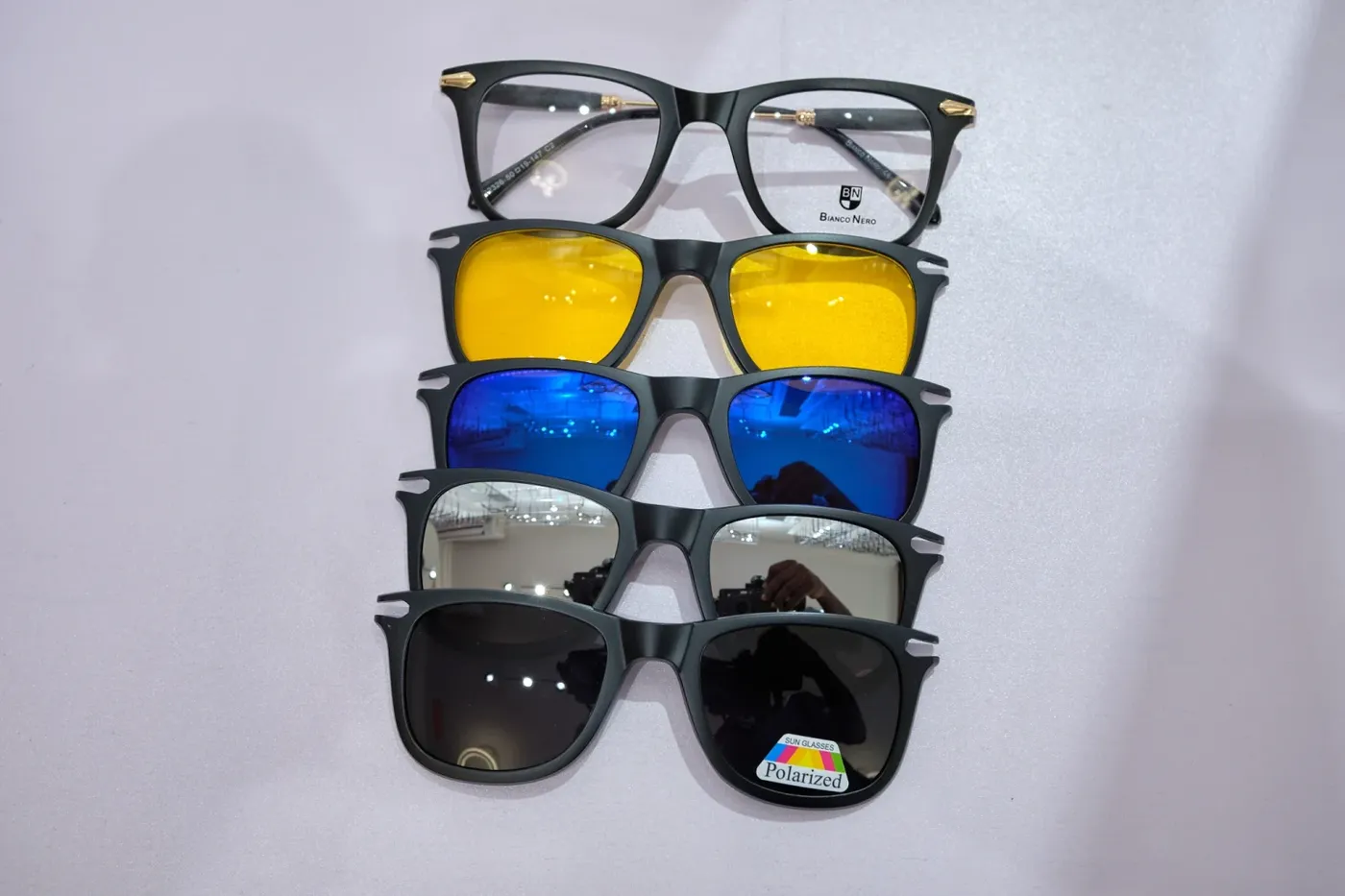 A pair of black Bianco Nero frames with four magnetic clip-on lenses in yellow, blue mirror, silver mirror and polarised grey